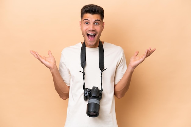 Junger Fotograf, kaukasischer Mann isoliert auf beigem Hintergrund mit schockiertem Gesichtsausdruck