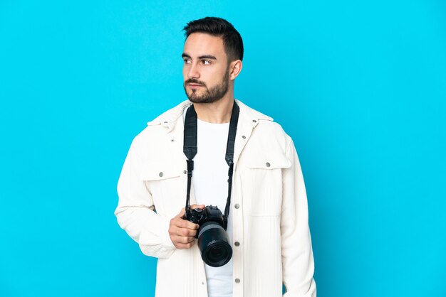 Junger Fotograf Mann isoliert auf blauem Hintergrund, der zur Seite schaut