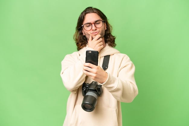 Foto junger fotograf mit isoliertem hintergrund denkt nach und sendet eine nachricht