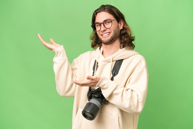 Junger Fotograf mit isoliertem Hintergrund, der die Hände zur Seite streckt, um zum Kommen einzuladen