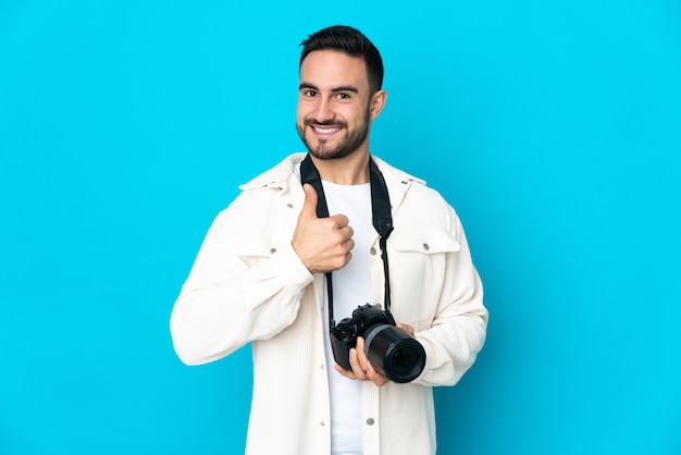 Junger Fotografmann lokalisiert auf blauem Hintergrund, der eine Daumen hoch Geste gibt