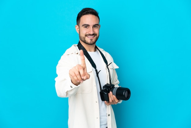 Junger Fotografmann lokalisiert auf blauem Hintergrund, der einen Finger zeigt und hebt