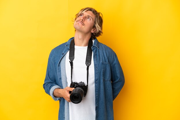 Junger Fotografmann lokalisiert auf gelbem Hintergrund und nach oben schauend