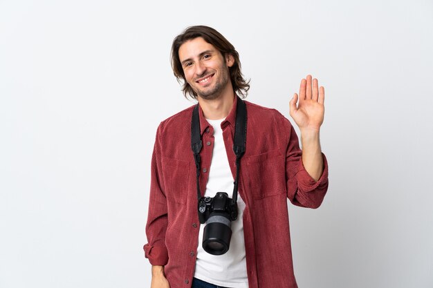 Junger Fotografmann lokalisiert auf weißem Hintergrund, der mit Hand mit glücklichem Ausdruck salutiert