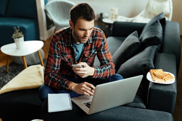 Junger Freiberufler, der Computer verwendet, während er zu Hause arbeitet.