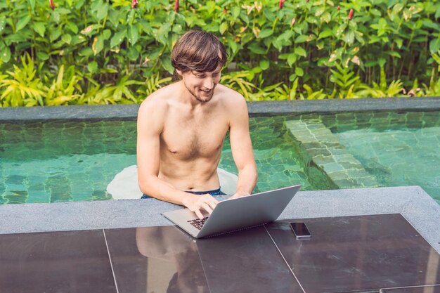 Junger Freiberufler, der im Urlaub neben dem Schwimmbad arbeitet.