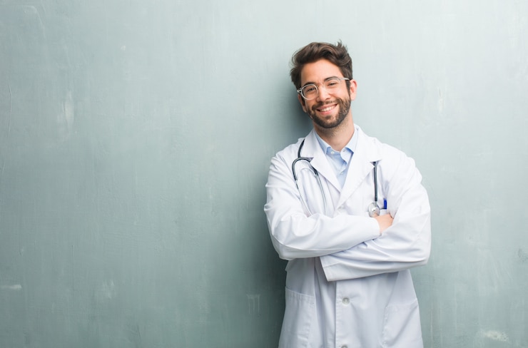Foto junger freundlicher doktormann gegen eine grunge wand mit einem exemplarplatz, der seine arme kreuzt