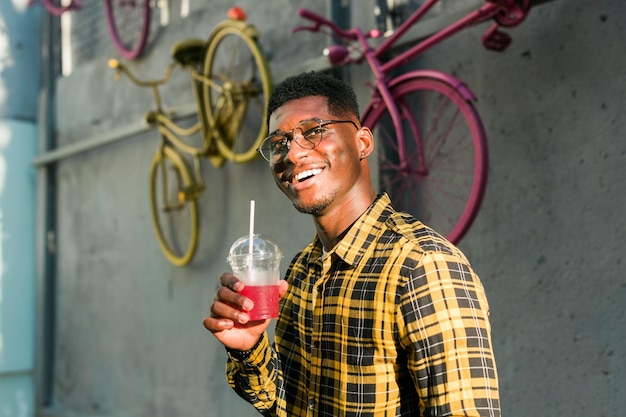 Junger fröhlicher afrikanisch-amerikanischer Mann in der Stadt, der Spaß hat und einen Cocktail hält Mann im Sommerurlaub Freizeit-Lifestyle-Urlaub und Sommergetränke-Konzept