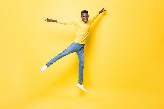 Junger, fröhlicher, energischer afrikanischer Mann, der mit offenen Armen und Beinen auf isoliertem gelbem Studiohintergrund springt