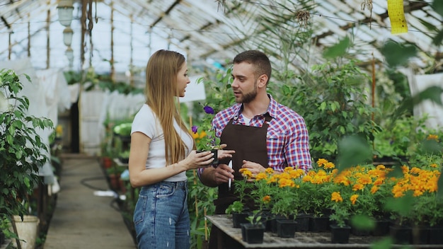 Junger fröhlicher Florist, der mit Kunden spricht und Ratschläge gibt, während er im Gartencenter arbeitet