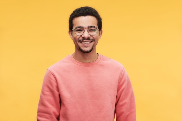 Junger fröhlicher Mann mit Brille und rosafarbenem Sweatshirt, der in die Kamera schaut