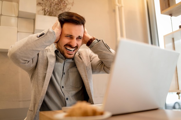 Junger frustrierter Geschäftsmann in einer Pause in einem Café. Er arbeitet am Laptop.