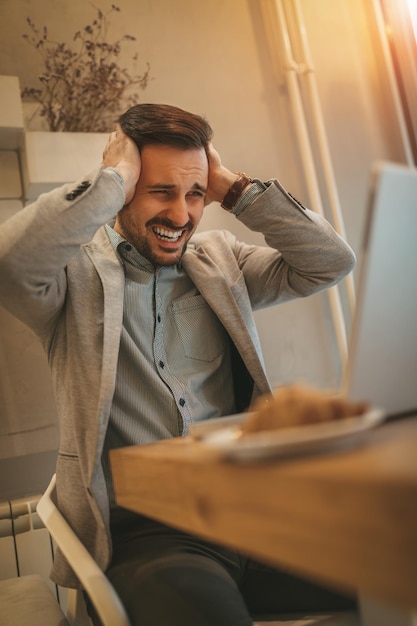 Junger frustrierter Geschäftsmann in einer Pause in einem Café. Er arbeitet am Laptop.