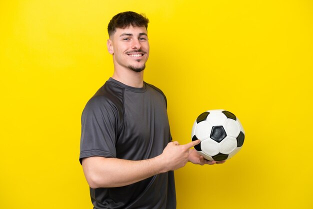 Junger Fußballspielermann lokalisiert auf gelbem Hintergrund, der zurück zeigt