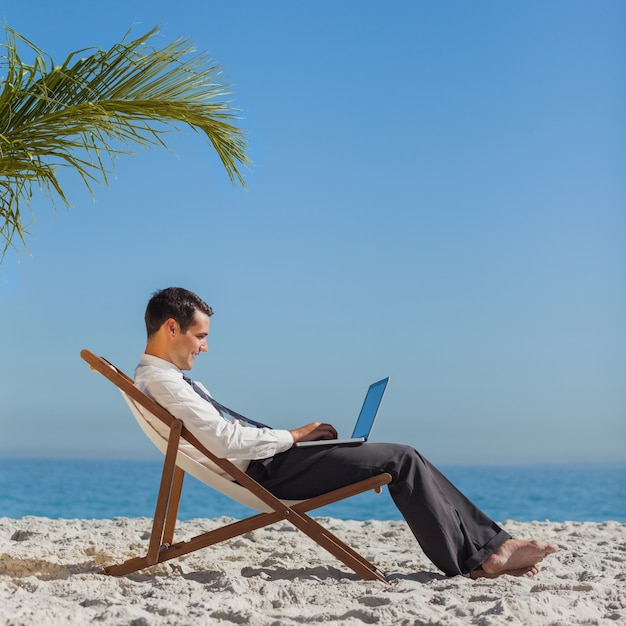 Junger Geschäftsmann auf seinem Strandstuhl unter Verwendung seines Laptops