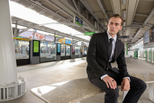 Junger Geschäftsmann, der am Bahnhof beim Denken sitzt