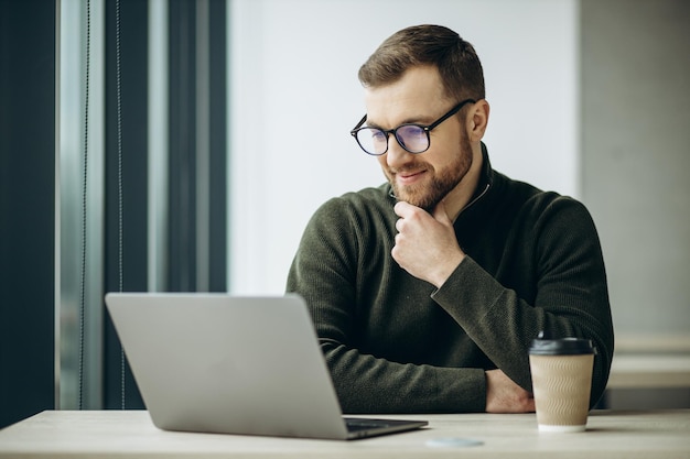 Junger Geschäftsmann, der am Computer arbeitet und im Büro Kaffee trinkt