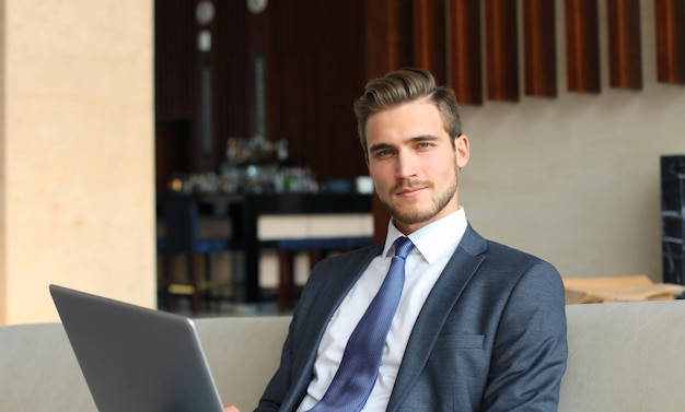 Junger Geschäftsmann, der am Laptop arbeitet, in der Hotellobby sitzt und auf jemanden wartet?