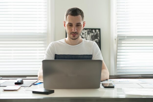 Junger Geschäftsmann, der an einem Laptop an seinem Schreibtisch im Büro arbeitet