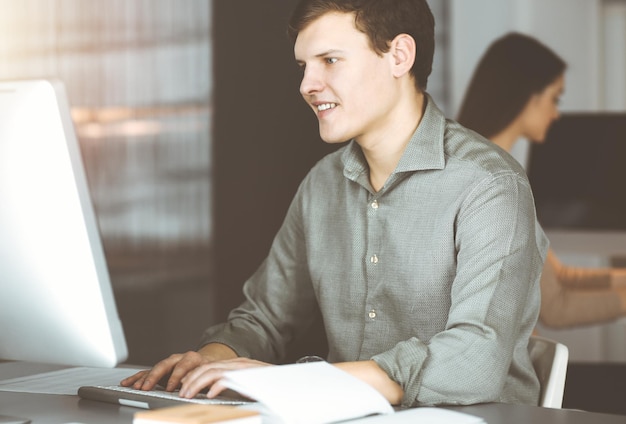 Junger Geschäftsmann, der an seinem Computer arbeitet und am Schreibtisch im Büro sitzt. Headshot-Porträt eines Mannes