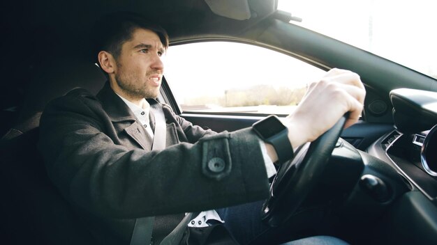 Junger Geschäftsmann, der Auto fährt, sehr verärgert und gestresst, nachdem er hart versagt und sich im Stau bewegt hat