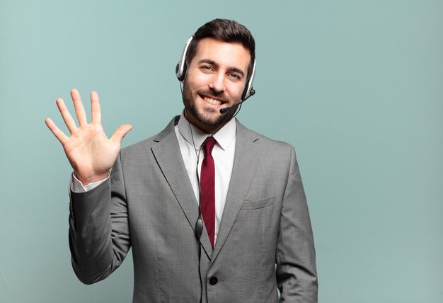 Junger Geschäftsmann, der freundlich lächelt und schaut, Nummer fünf oder fünften mit Hand vorwärts zeigend, Telemarketing-Konzept herunterzählend