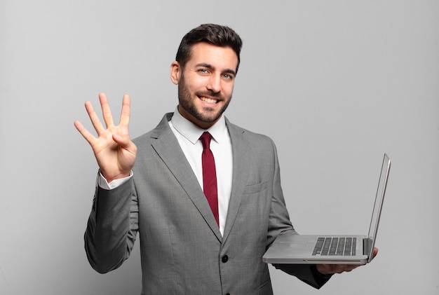 Junger Geschäftsmann, der freundlich lächelt und schaut, Nummer vier oder vierten mit der Hand vorwärts zeigend, herunterzählend und einen Laptop haltend