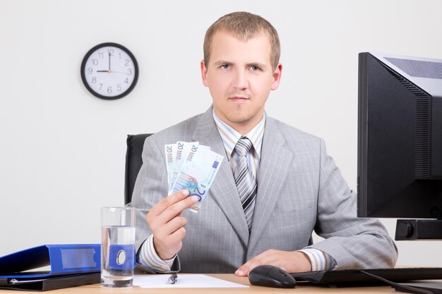 Foto junger geschäftsmann, der geld im hellen büro zeigt