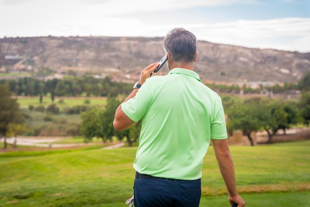 Junger Geschäftsmann, der Golf spielt und einen Arbeitsanruf mit dem Telefon des Clubs beantwortet