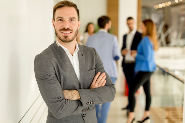 Junger Geschäftsmann, der im Büro und in anderen jungen Geschäftsleuten sprechen im Hintergrund steht