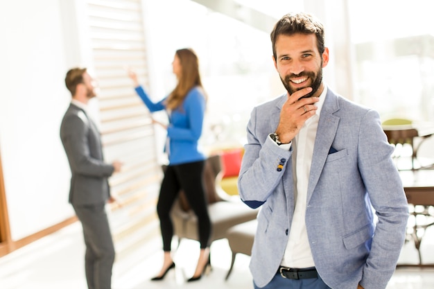 Junger Geschäftsmann, der im Büro und in anderen jungen Geschäftsleuten sprechen im Hintergrund steht