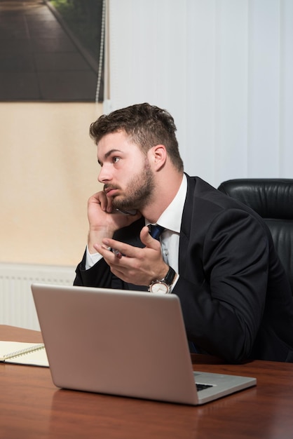 Junger Geschäftsmann, der in seinem Büro arbeitet, während er am Telefon spricht