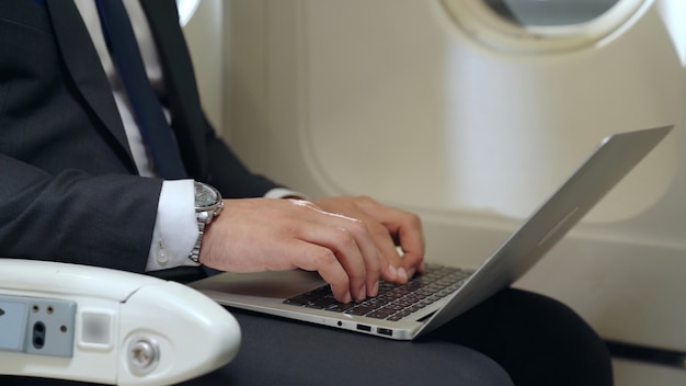 Junger Geschäftsmann, der Laptop im Flugzeug verwendet