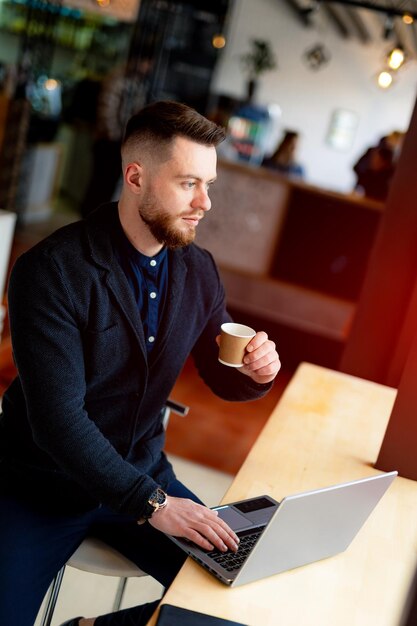 Junger Geschäftsmann, der mit Laptop auf Distanz arbeitet Gutaussehender, intelligenter Mann hat eine Arbeit im Café, während er Kaffee trinkt Hoher Winkel