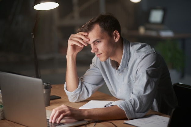 Junger Geschäftsmann, der nachts allein in seinem Büro arbeitet