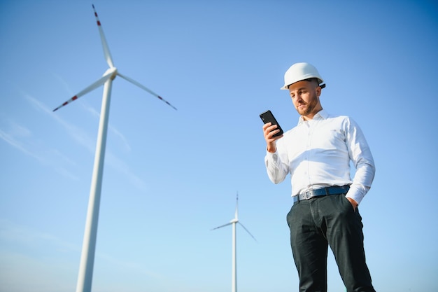 Junger Geschäftsmann im Gespräch mit Manager über intelligentes Telefon auf Windkraftanlagenfeld, Green Energy Concept