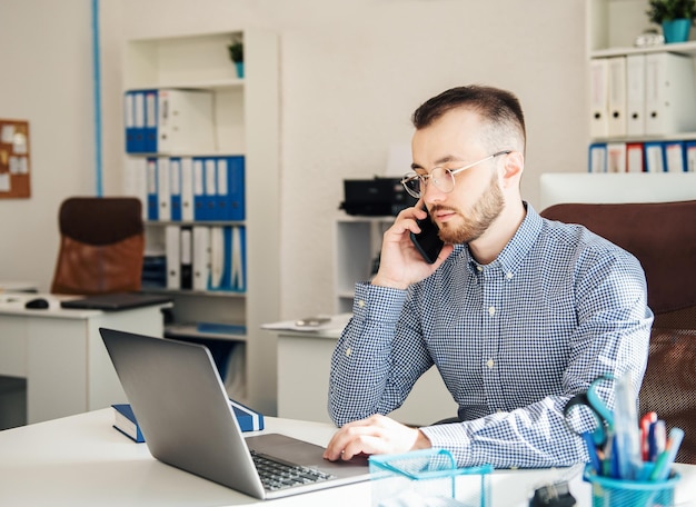 Junger Geschäftsmann im Hemd, der an seinem Laptop in einem Büro arbeitet