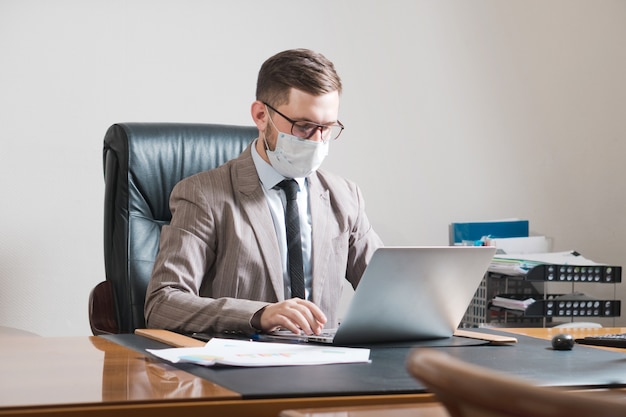 Junger Geschäftsmann in Brille und Gesichtsmaske im Büro