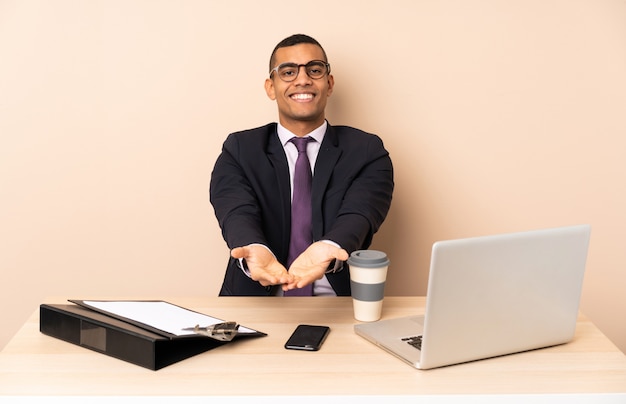 Junger Geschäftsmann in seinem Büro mit einem Laptop und anderen Dokumenten, die copyspace eingebildet auf der Palme halten, um eine Anzeige einzufügen