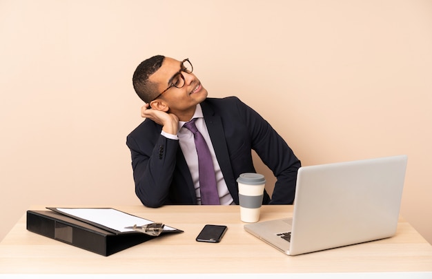 Junger Geschäftsmann in seinem Büro mit einem Laptop und anderen Dokumenten, die eine Idee denken