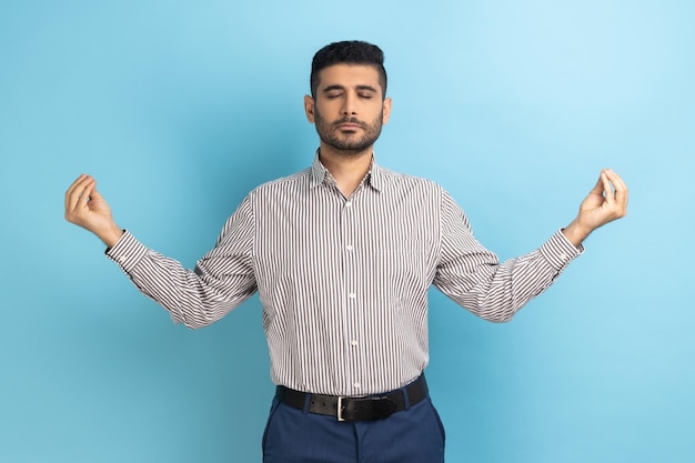 Junger Geschäftsmann mit Bart, der mit erhobenen Armen steht und Yoga-Meditationsübungen macht