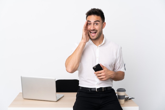 Junger Geschäftsmann mit einem Mobiltelefon an einem Arbeitsplatz, der mit offenem Mund schreit