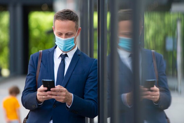 Junger Geschäftsmann mit Maske mit Telefon im Freien