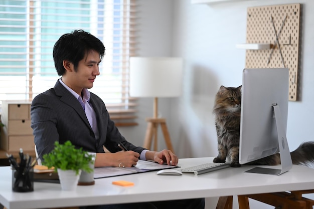 Junger Geschäftsmann mit seiner Katze, während er in seinem Haus aus der Ferne mit dem Computer arbeitet