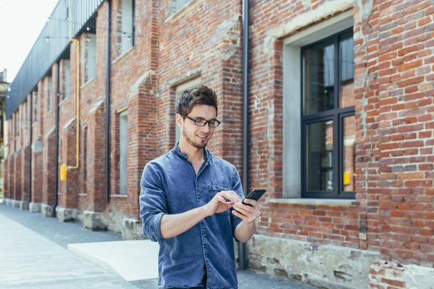 Junger Geschäftsmann nutzt Telefon außerhalb des Büros glücklicher und lächelnder Mann mit Smartphone