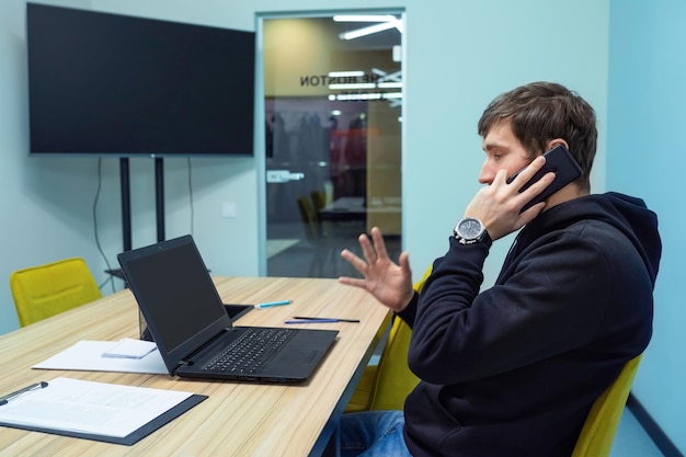 Junger Geschäftsmann sitzt am Bürotisch und telefoniert