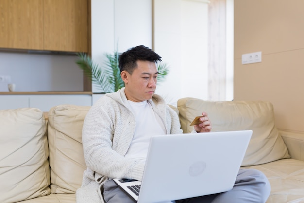 junger glücklicher asiatischer mann, der online im internetshop mit laptop-computer und kreditkarte einkauft