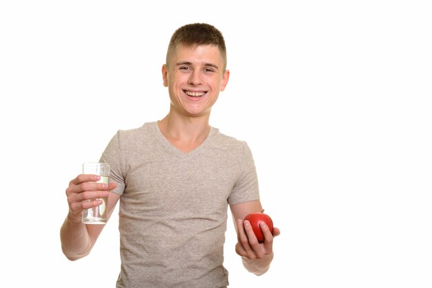 Junger glücklicher kaukasischer Mann, der lächelt, während er Glas Wasser und roten Apfel hält