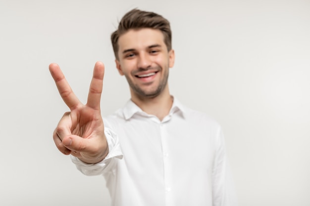 Foto junger glücklicher mann auf weißem hintergrund lächelnd mit zwei fingern auf kamerafokus auf der hand