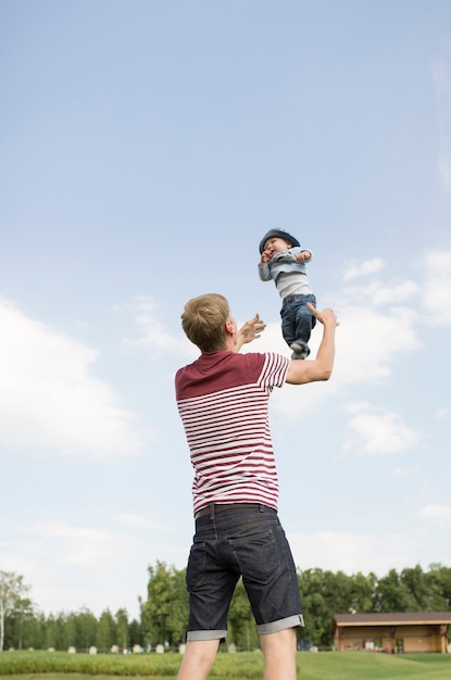 junger glücklicher Papa, der seinen kleinen Sohn in die Luft wirft und Spaß zusammen hat.